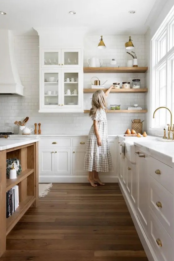 a cozy modern kitchen with white cabinets, light stained shelves, a light stained kitchen island, brass sconces and fixtures is chic