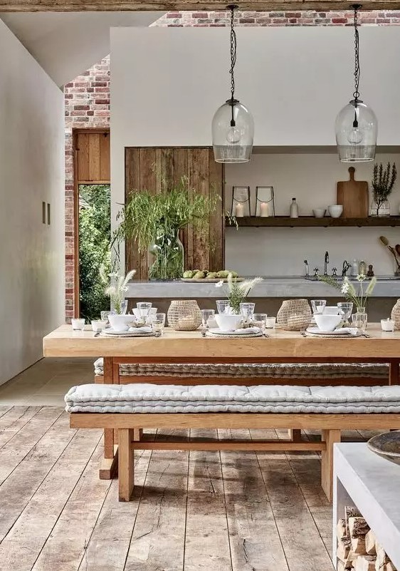 a cozy rustic dining room wiht a wooden beam, a table with a stone tabletop, wooden benches with cushions and glass pendant lamps