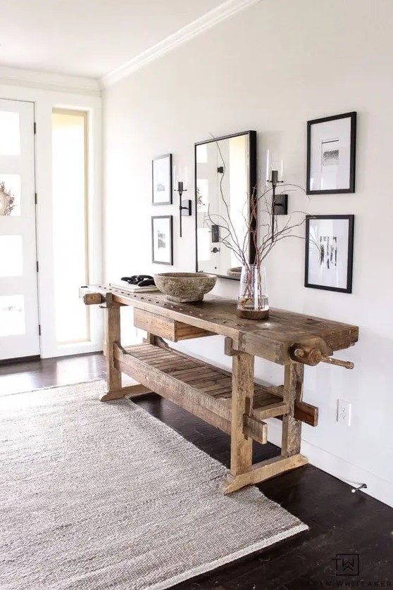 a delicate and airy greige entryway with a mini gallery wall with black frames, a stained vintage table, a neutral rug and lots of natural light