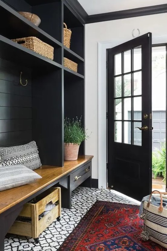 a farmhouse black and white entryway with a printed tile floor, a black storage unit with baskets, a bench and some potted plants