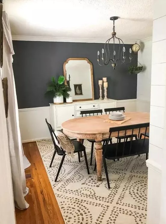 a farmhouse dining room with a grey accent wall, a vintage wooden dining table, black chairs and a bench, a vintage chandelier and a sideboard with some decor