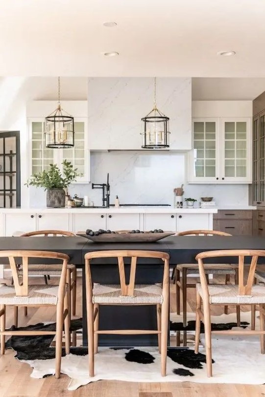 a farmhouse dining space with a black dining table, stained wishbone chairs, a cowhide rug and a kitchen zone next to it