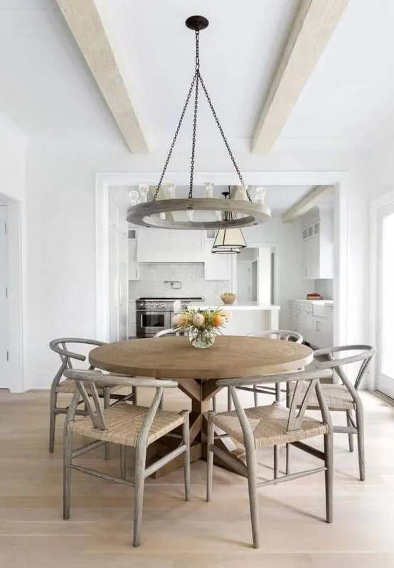 a farmhouse dining space with a large wooden dining table and grey wishbone chairs, a heavy round chandelier is cool and cozy