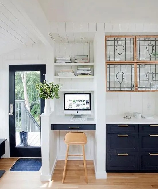 a farmhouse kitchen with navy cabinets, a small nook with a built-in desk, built-in shelves, a light-stained stool and potted greenery