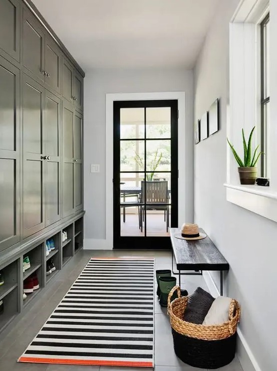 a farmhouse mudroom with a black storage unit, a striped rug, a black bench and a basket with pillows