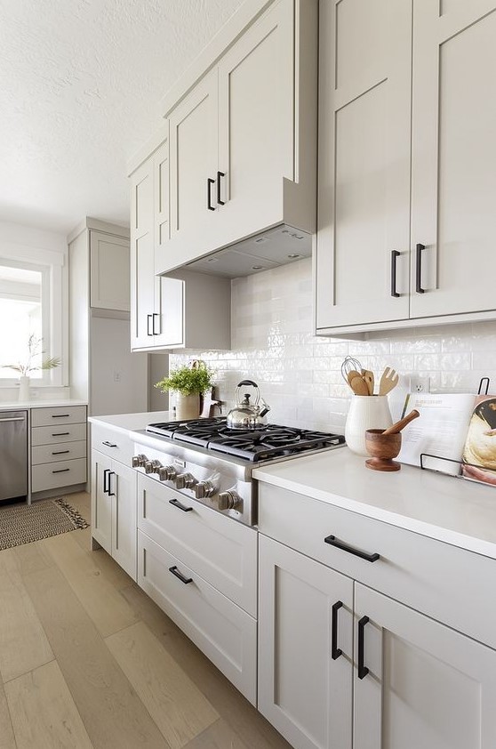 a grey farmhosue kitchen with shaker style cabinets, a white tile backsplash and white countertops plus black fixtures