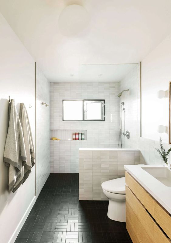 a laconic modern farmhouse bathroom with a black floor and marble tile walls, a timber vanity, a shower space and a window