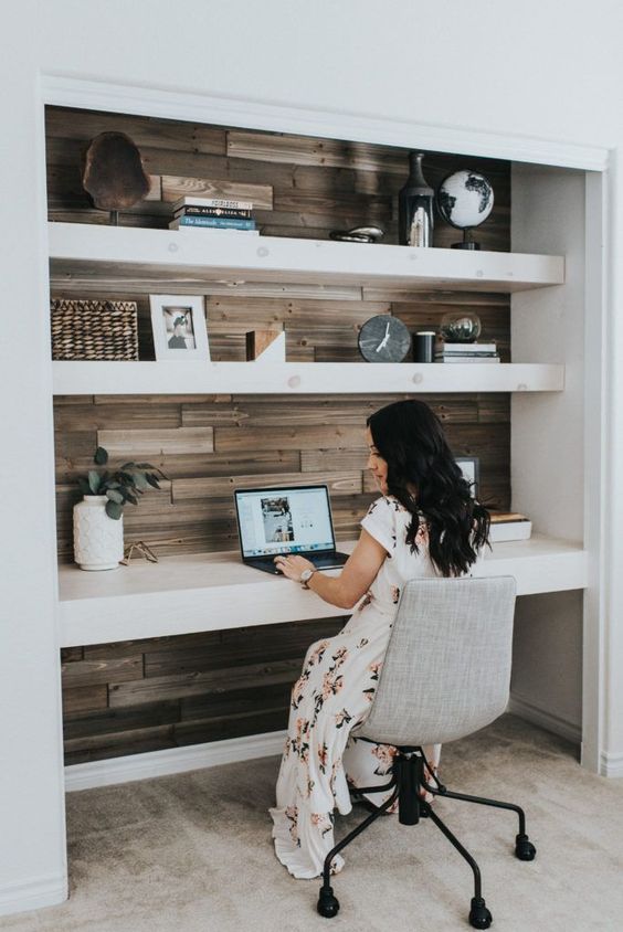 a large niche covered with wood, with built-in shelves and a desk, some pretty decor, a laptop and a chair on casters