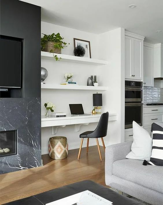 a large niche with built-in shelves and a desk with drawers, potted greenery and blooms, table lamps, vases and a black chair