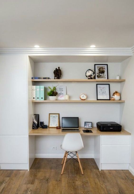 a large niche with built-in shelves and a desk with drawers, some books, candles, artwork and a laptop