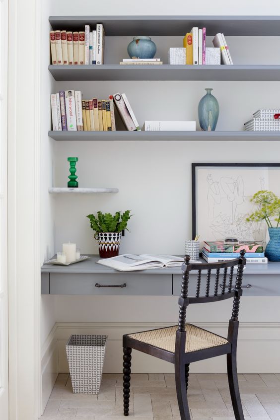 a large niche with built-in shelves and a desk with drawers, some books, vases and decor and an elegant vintage chair