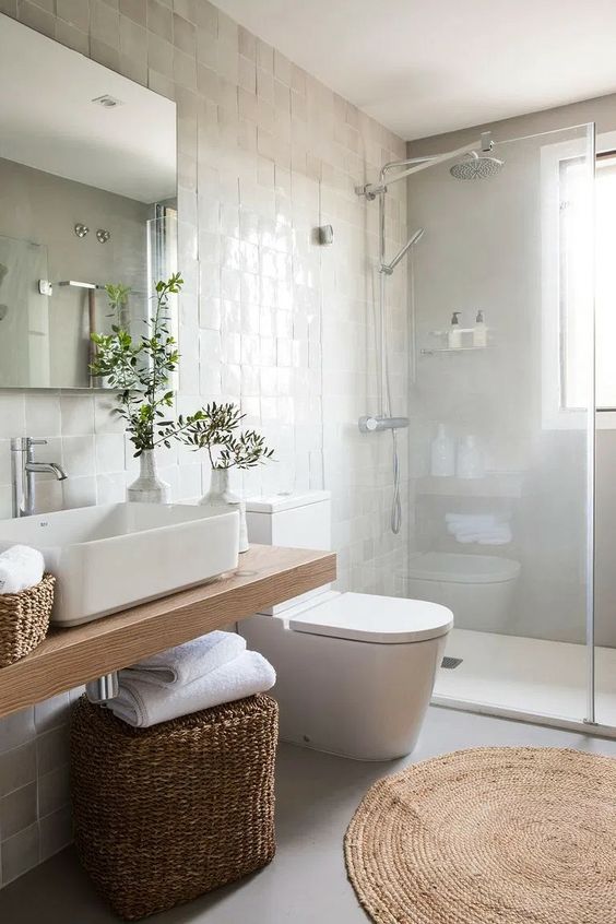 a lovely modern farmhouse bathroom with neutral Zellige tiles, a wall-mounted vanity, a jute rug, baskets for storage