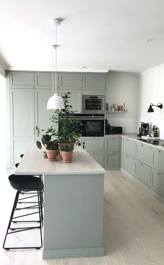 a lovely pale green modern country kitchen with neutral countertops and tall black stools and sconces is a chic room