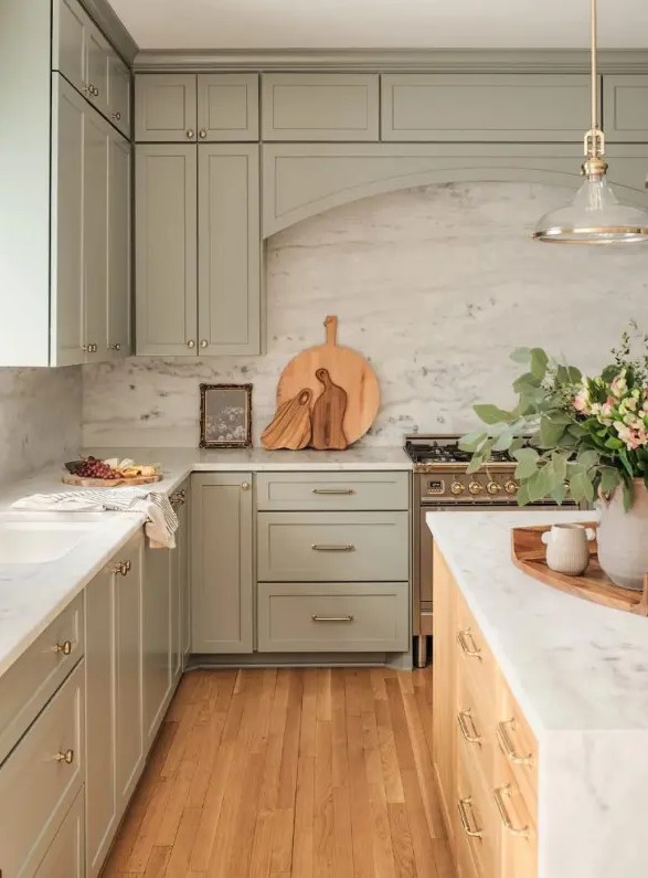 a lovely sage green kitchen with shaker cabinets, a white stone backsplash and countertops, a stained kitchen island and a chic pendant lamp