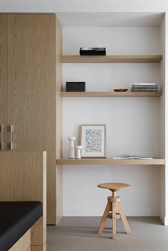 a minimalist awkward nook with built-in shelves and a desk, with a wooden stool and books plus candle lanterns is amazing