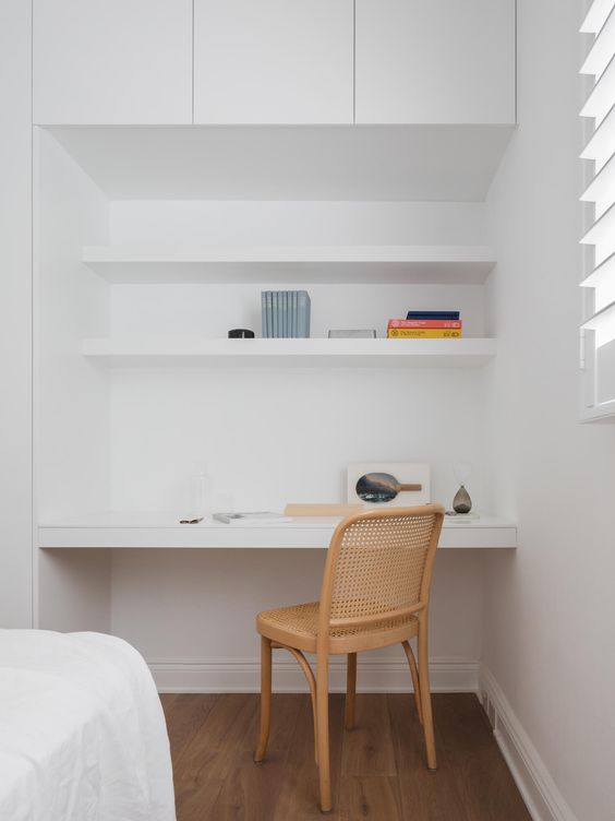 a minimalist niche with built-in shelves and a desk, some books and a cane chair is a lovely nook to squeeze into a bedroom