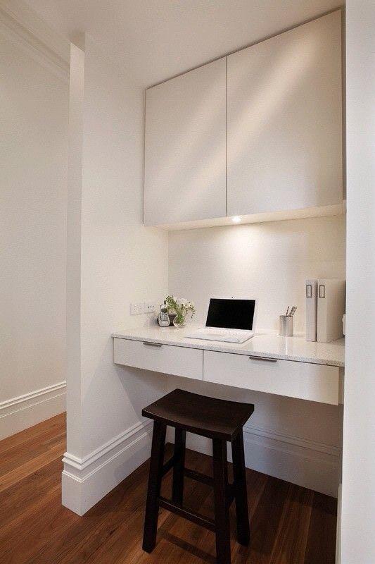 a minimalist nook with a built-in cabinet and a desk with drawers, built-in lights, a black stool and some blooms