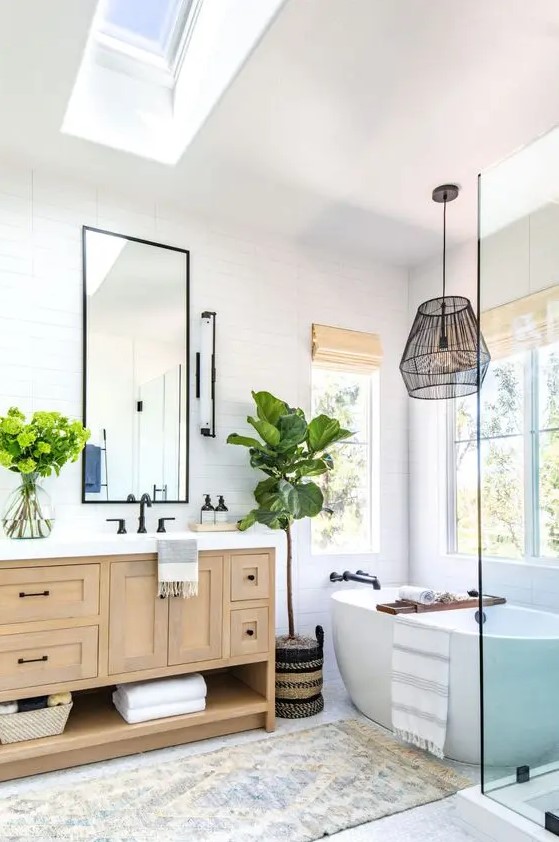 a modern country bathroom with white skinny tiles, a stained vanity, an oval tub, a pendant lamp and a skylight