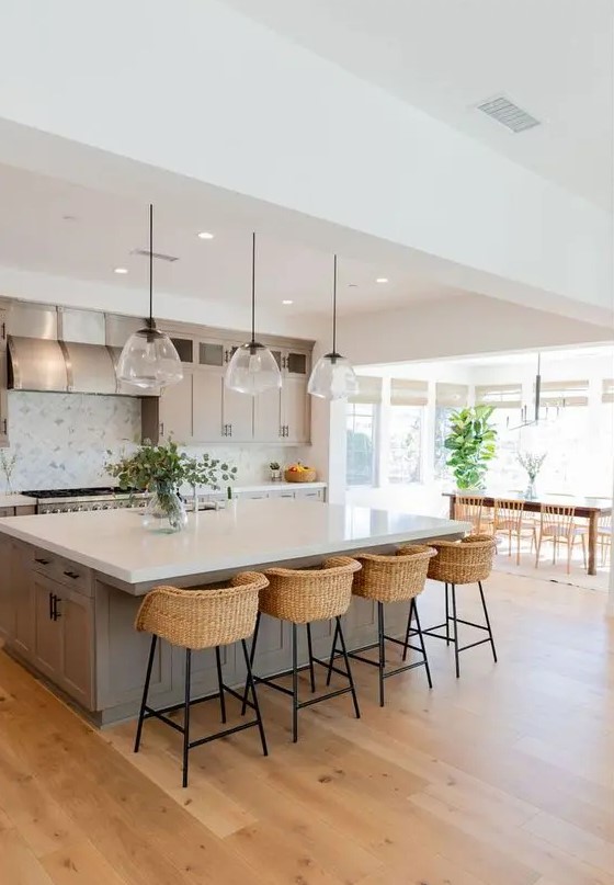 a modern country kitchen in dove grey, with shaker style cabinets, a large kitchen island, pendant lamp, woven stools