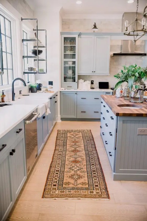 a modern country kitchen in light blue, with shaker style cabinets, white and butcherblock countertops, an open metal shelf and a metal hood