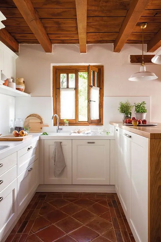 a modern country kitchen with a tiled floor, white cabinets and a raised butcherblock countertops, a wooden ceiling with beams and frames on the window