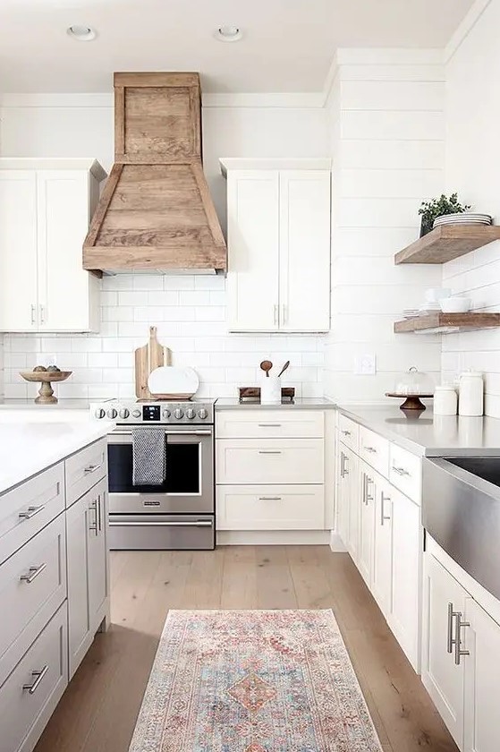 a modern country kitchen with shaker style cabinets, a white subway tile backsplash, a wooden hood and floating shelves