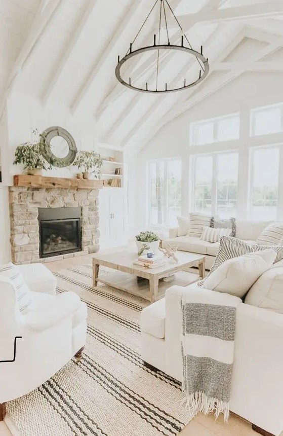 a modern country living room designed in neutrals, with a fireplace clad with stone, cozy furniture and printed textiles