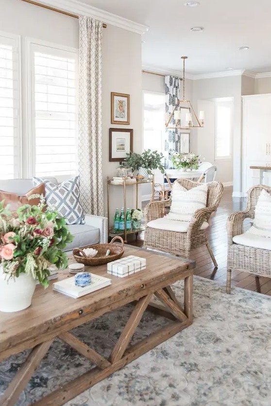 a modern country living room in neutrals, with a creamy sofa, woven chairs, a low coffee table, printed textiles and potted plants