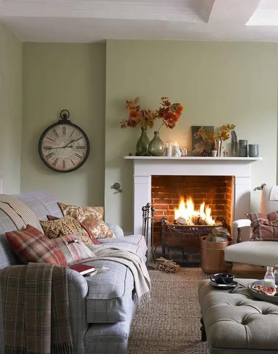 a modern country living room with light green walls, a fireplace, neutral furniture and printed textiles, a vintage clock and leaves