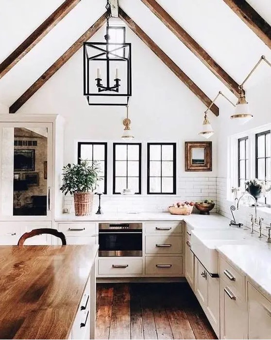 a modern dove grey country kitchen with dark wooden beams on the ceiling, pendant lamps and a kitchen island with a butcherblock countertop