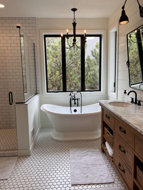 a modern farmhouse bathroom with subway and hex tiles, shiplap walls, a stained vanity, black lamps and a view of the forest