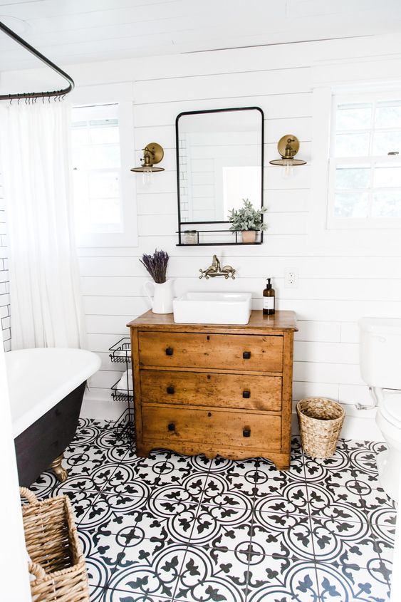 a modern farmhouse bathroom with white shiplap walls, a black printed tile floor, a vintage dresser vanity, a black tub and baskets