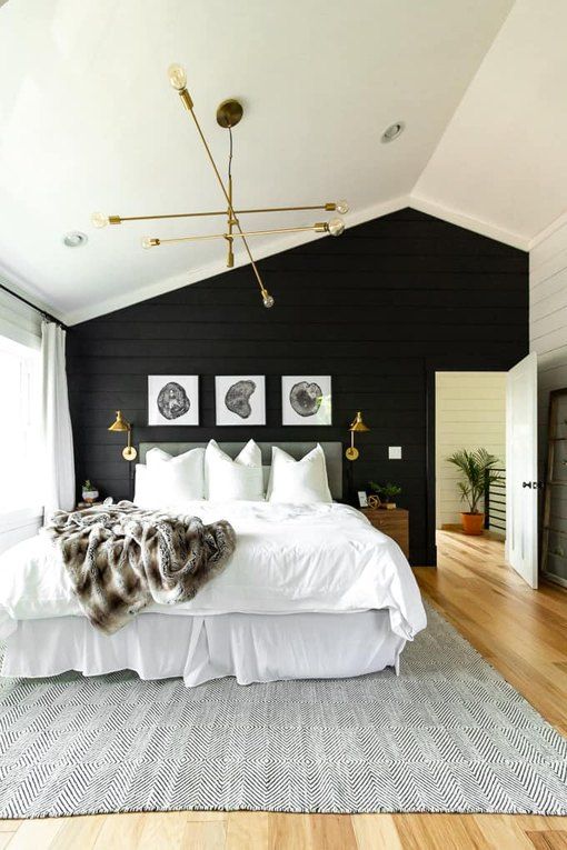 A Modern Farmhouse Bedroom With A Black Accent Wall A Grey Upholstered Bed With Neutral Bedding A Mini Gallery Wall A Gold Chandelier 