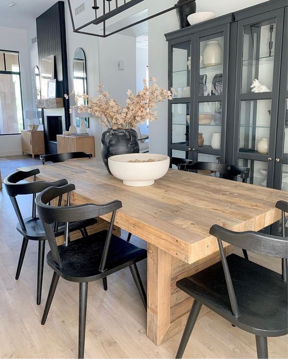 a modern farmhouse dining room with a black glazed cupboard, a heavy stained table, black chairs and a black framed chandelier