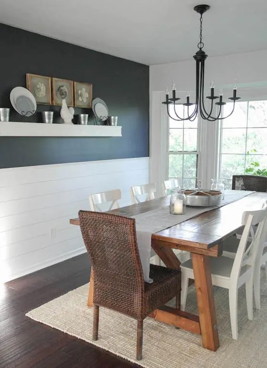 a modern farmhouse dining room with a black wall and white planks, a stained dining table, mismatching chairs and a vintage chandelier