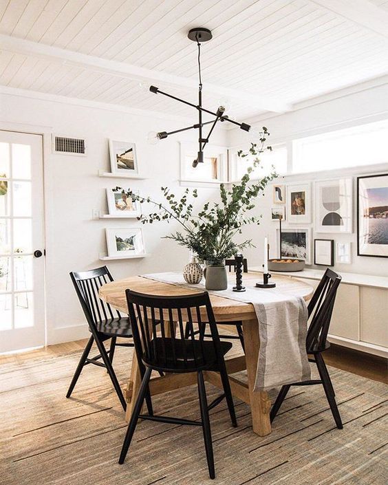 a modern farmhouse dining room with a credenza, a round stained table, black chairs, ledges and a free form gallery wall