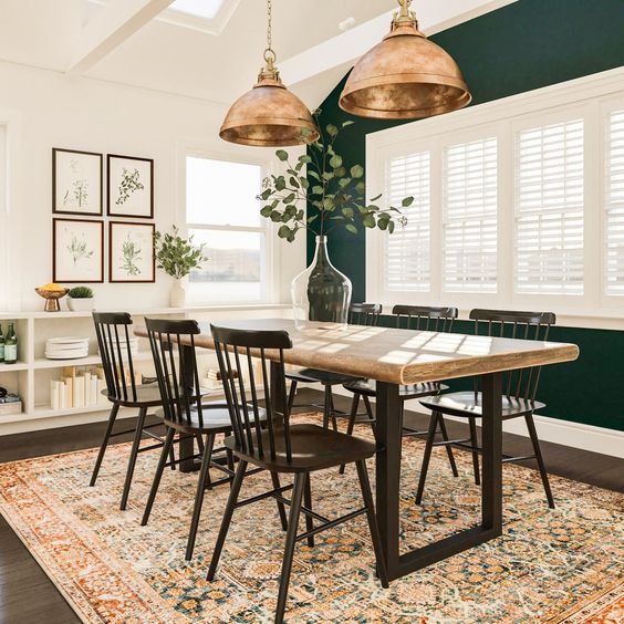 a modern farmhouse dining room with a forest green accent wall, a table with a wooden tabletop, black chairs, an IKEA storage unit and elegant brass pendant lamps