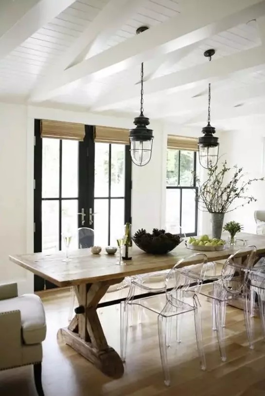 a modern farmhouse dining room with a wooden table, wicker shades, ghost chairs, vintage lanterns and black doors