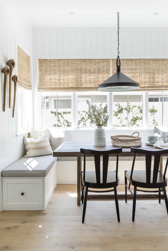 a modern farmhouse dining space with a corner banquette seating, a stained table and black chairs, a black pendant lamp