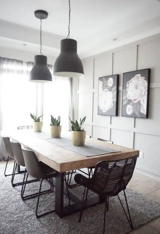 a modern farmhouse dining space with a grey paneled accent wall, a dining table with a thick tabletop, mismatching chairs and blakc pendant lamps