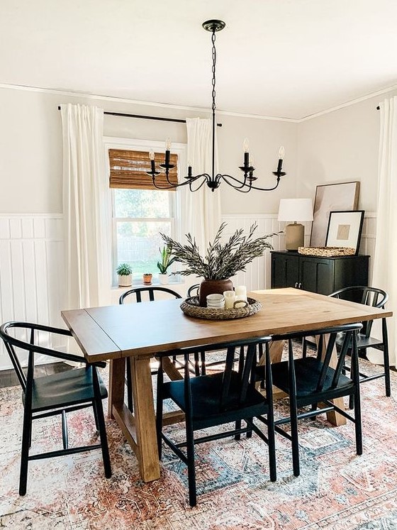 a modern farmhouse dining space with a stained table, black chairs, a black cabinet, a vintage chandelier and a printed rug