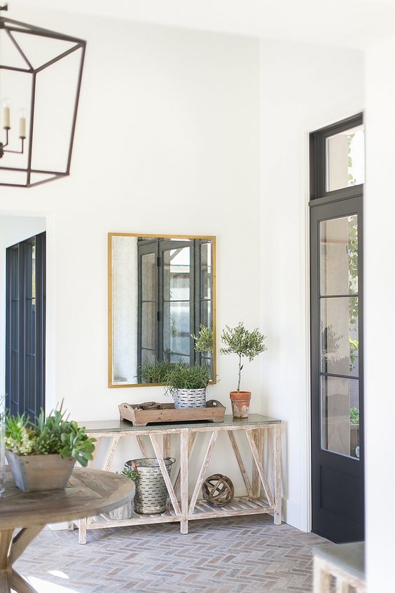 a modern farmhouse entry with a brick floor, a console table with buckets and greenery, a stained table and a frame lamp