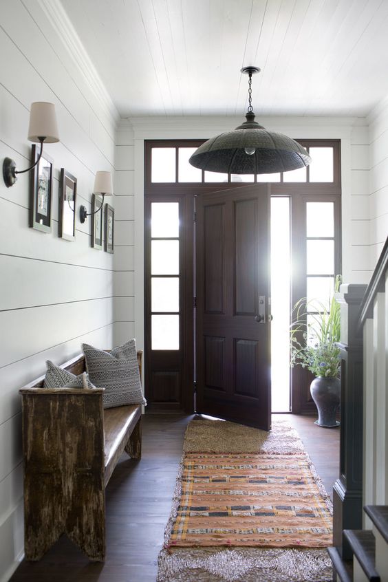 a modern farmhouse entry with a stained bench with pillows, a gallery wall, greenery in a vase and a pendant lamp