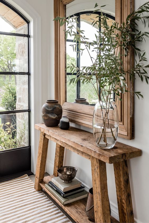 a modern farmhouse entryway with a large stained frame mirror, a console table, some vases and books and greenery