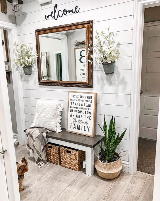 a modern farmhouse entryway with a shiplap wall, a wooden bench and baskets, a mirror, potted plants and lunaria arrangements