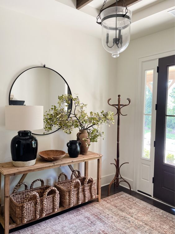 a modern farmhouse entryway with a stained console table, a couple of baskets, some lovely vases, a mirror and a rack