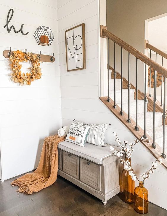 a modern farmhouse entryway with a storage bench, some amber bottles with cotton, a rack with a wreath and some decor on the walls