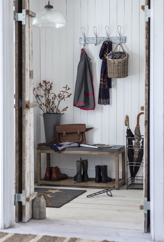 a modern farmhouse entryway with white shiplap walls, a bench, a rack, a bucket with branches and an umbrella stand