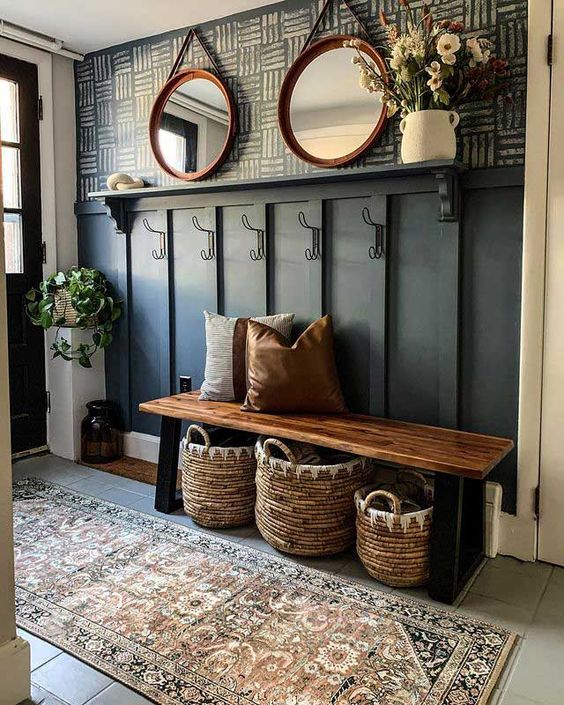 a modern farmhouse hallway with a black paneled wall, a bench, some baskets, potted greenery and blooms and round mirrors