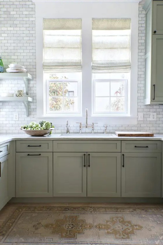 a modern farmhouse kitchen in sage green, with shaker cabinets, white stone countertops, white marble tiles and vintage fixtures